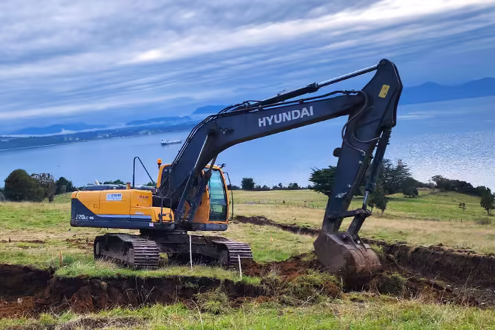 Retroexcavadora Hyundai realizando una zanja con el mar de fondo en Puerto Montt.