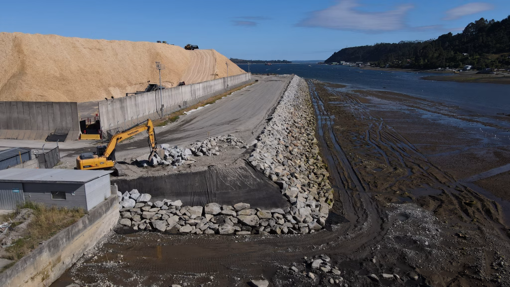 Vista general de la zona de trabajo en la ampliación del Puerto Punta Caullahuapi, mostrando el enrocado, el nuevo terreno conformado y maquinaria trabajando.