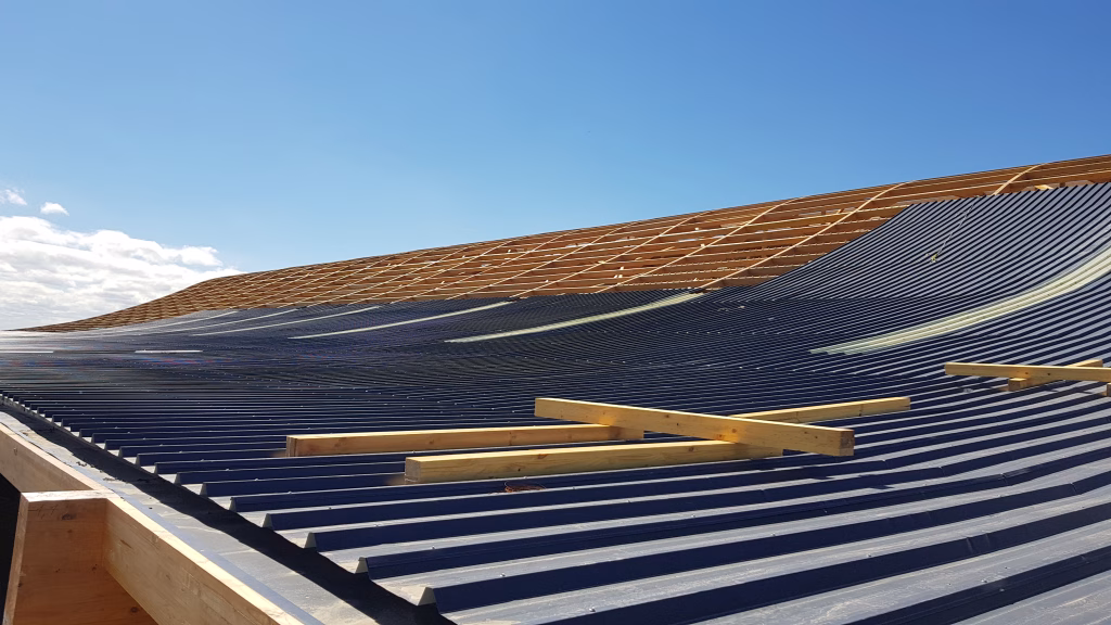 Fotografía del proceso de instalación de las placas metálicas en la techumbre de las Bodegas SQM, mostrando la estructura de madera y el avance del revestimiento.